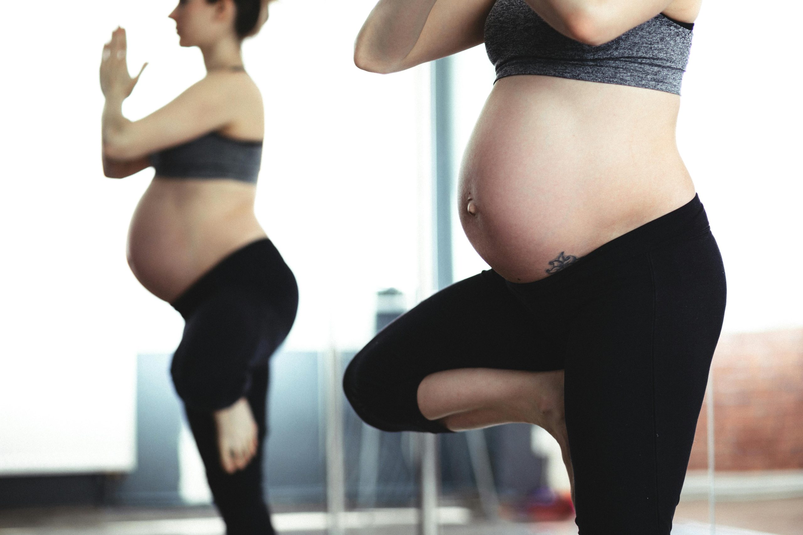 Pregnant woman doing yoga in front of mirror, promoting health and wellness.